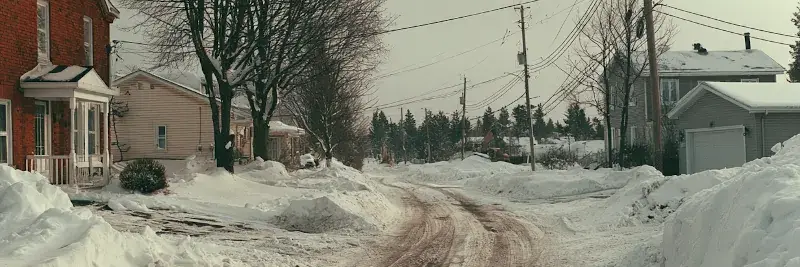 La même rue en milieu de matinée sous un ciel gris, chaussée dégagée et bancs de neige repoussés